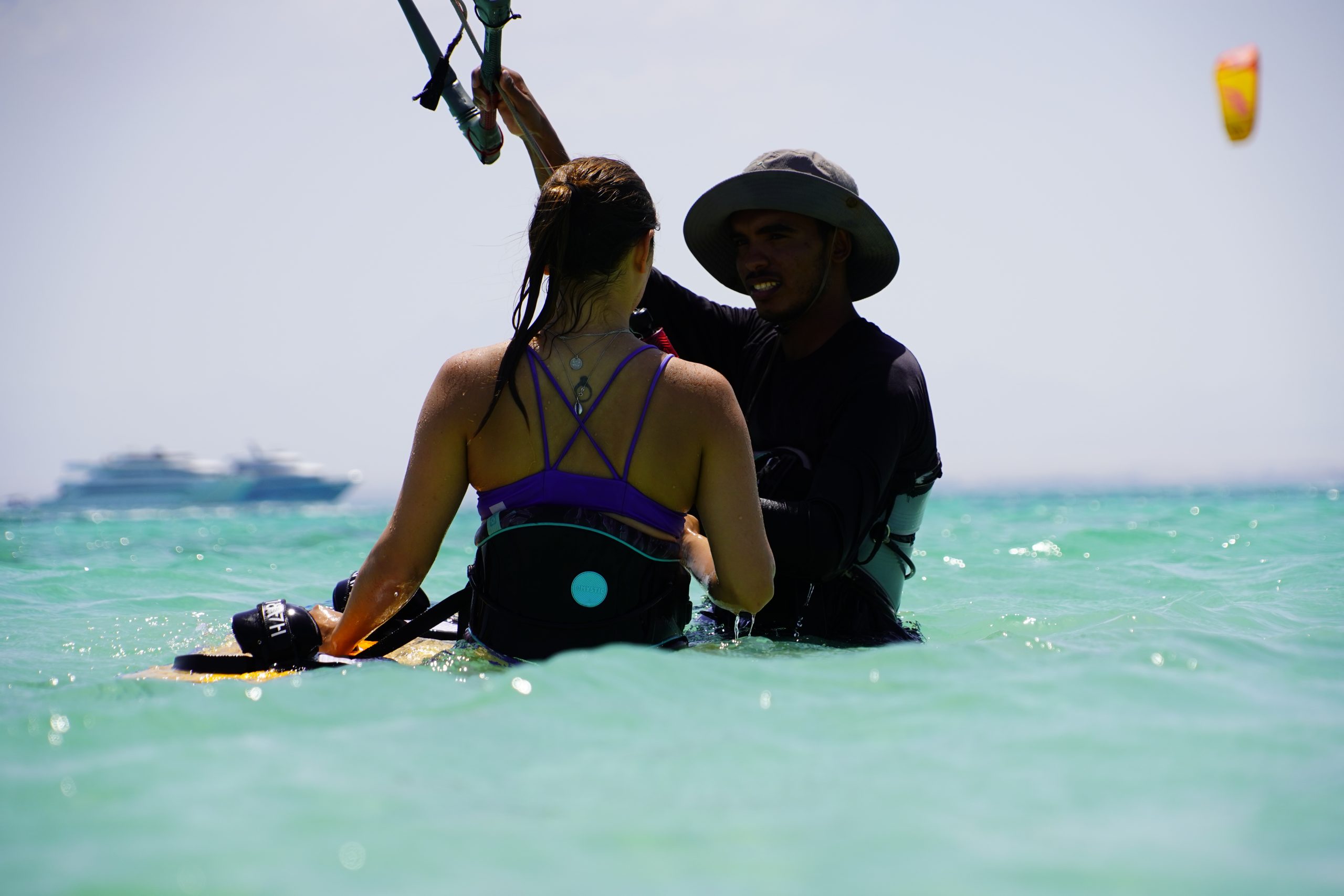 Kite-surfing-lessons-el-gouna group of 5 girls sitting on the kite beach in El Gouna in Egypt, looking at the kites in the water. The image shows the girls from the back, all wearing a Kite Tribe T-Shirt