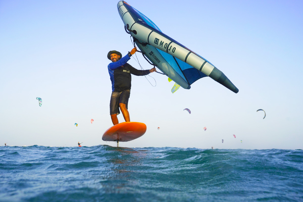 Wingfoiling lesson group of 5 girls sitting on the kite beach in El Gouna in Egypt, looking at the kites in the water. The image shows the girls from the back, all wearing a Kite Tribe T-Shirt