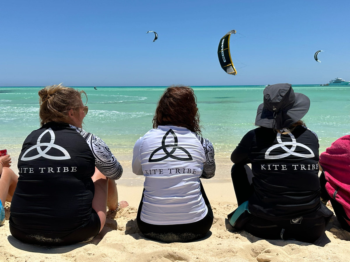 Kitetribe_kite_safari-beach group of people on the beach watching a kitesurfer jump. everyone is wearing a kite tribe tshirt