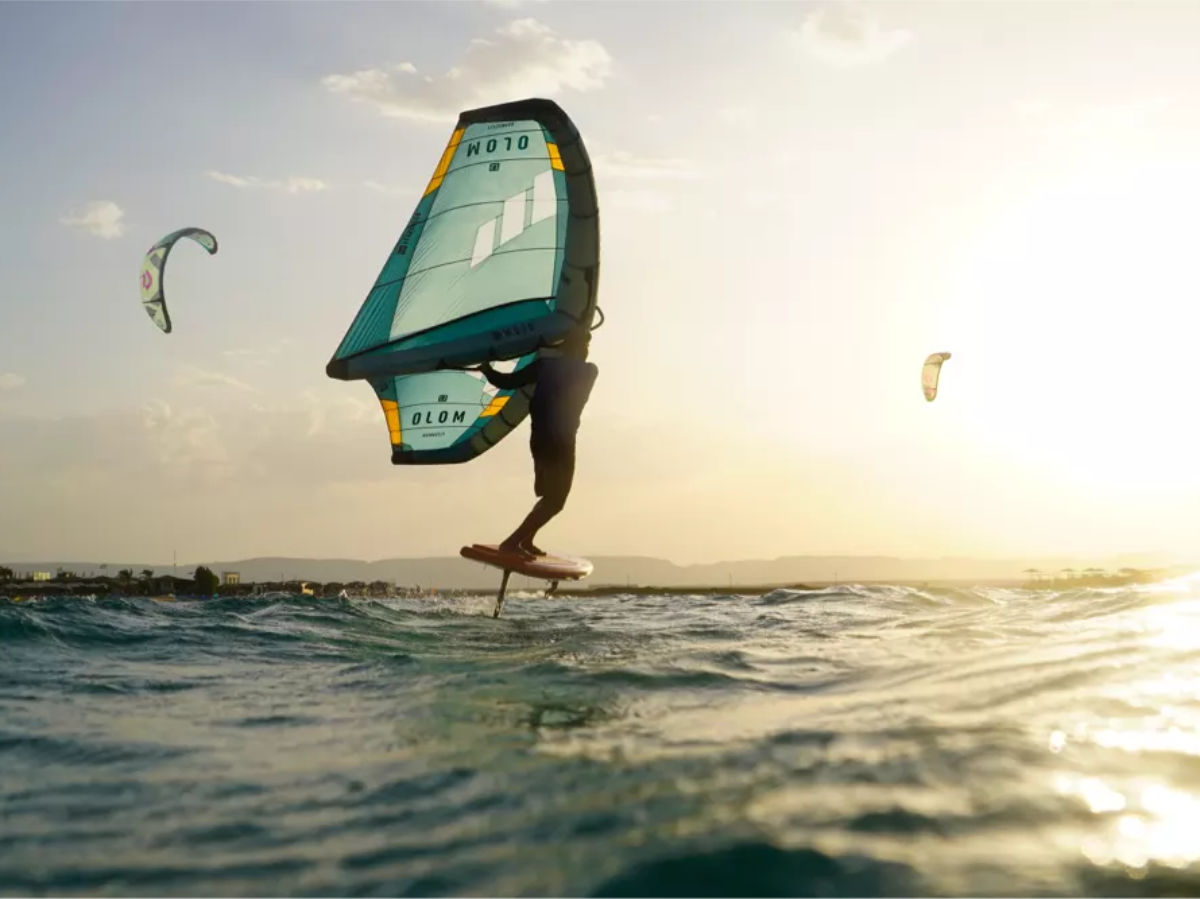 Wingfoil_hydrofoil-rental-1 group of people on the beach watching a kitesurfer jump. everyone is wearing a kite tribe tshirt