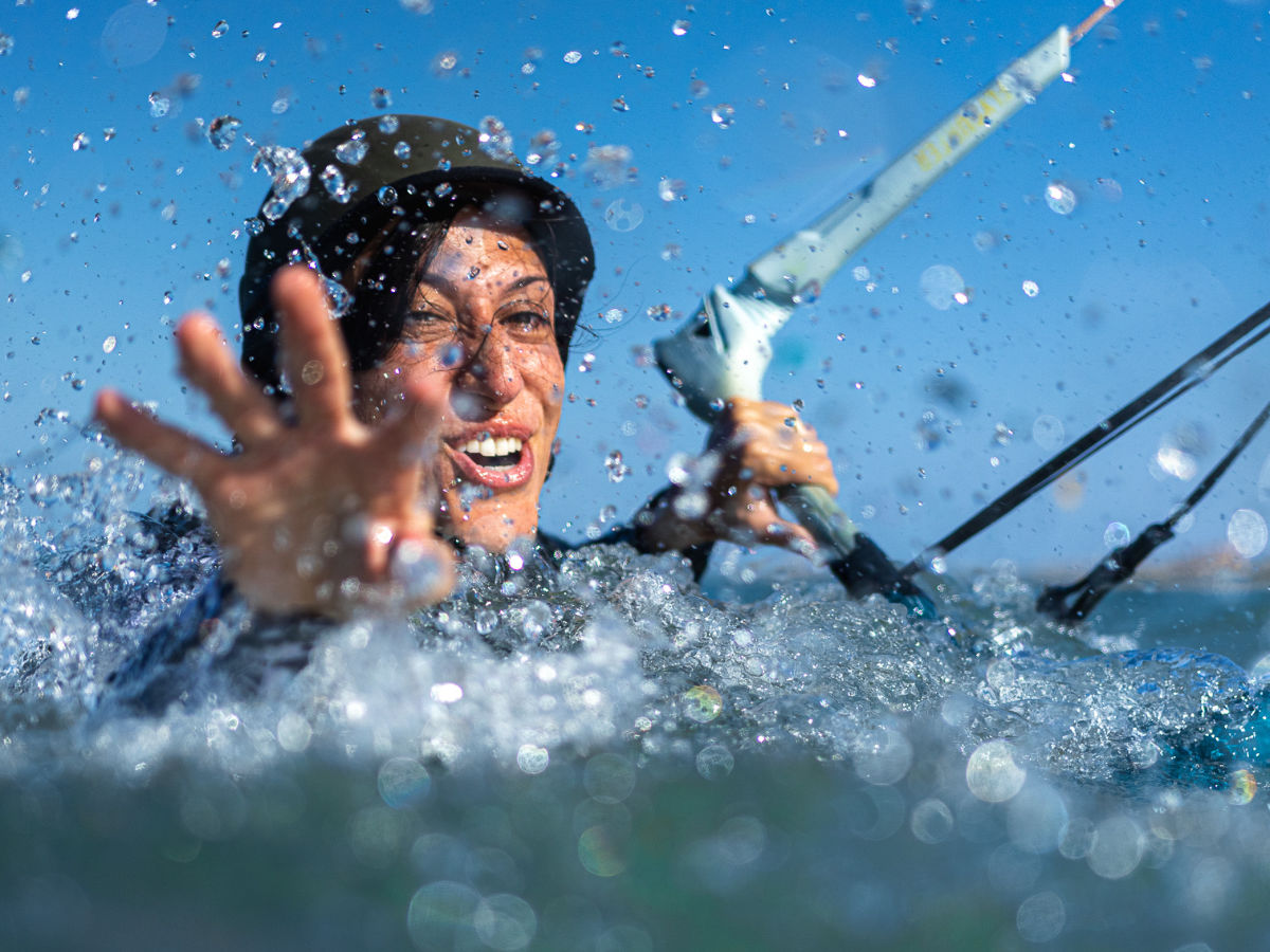 kitesurfing lesson splashes group of 5 girls sitting on the kite beach in El Gouna in Egypt, looking at the kites in the water. The image shows the girls from the back, all wearing a Kite Tribe T-Shirt