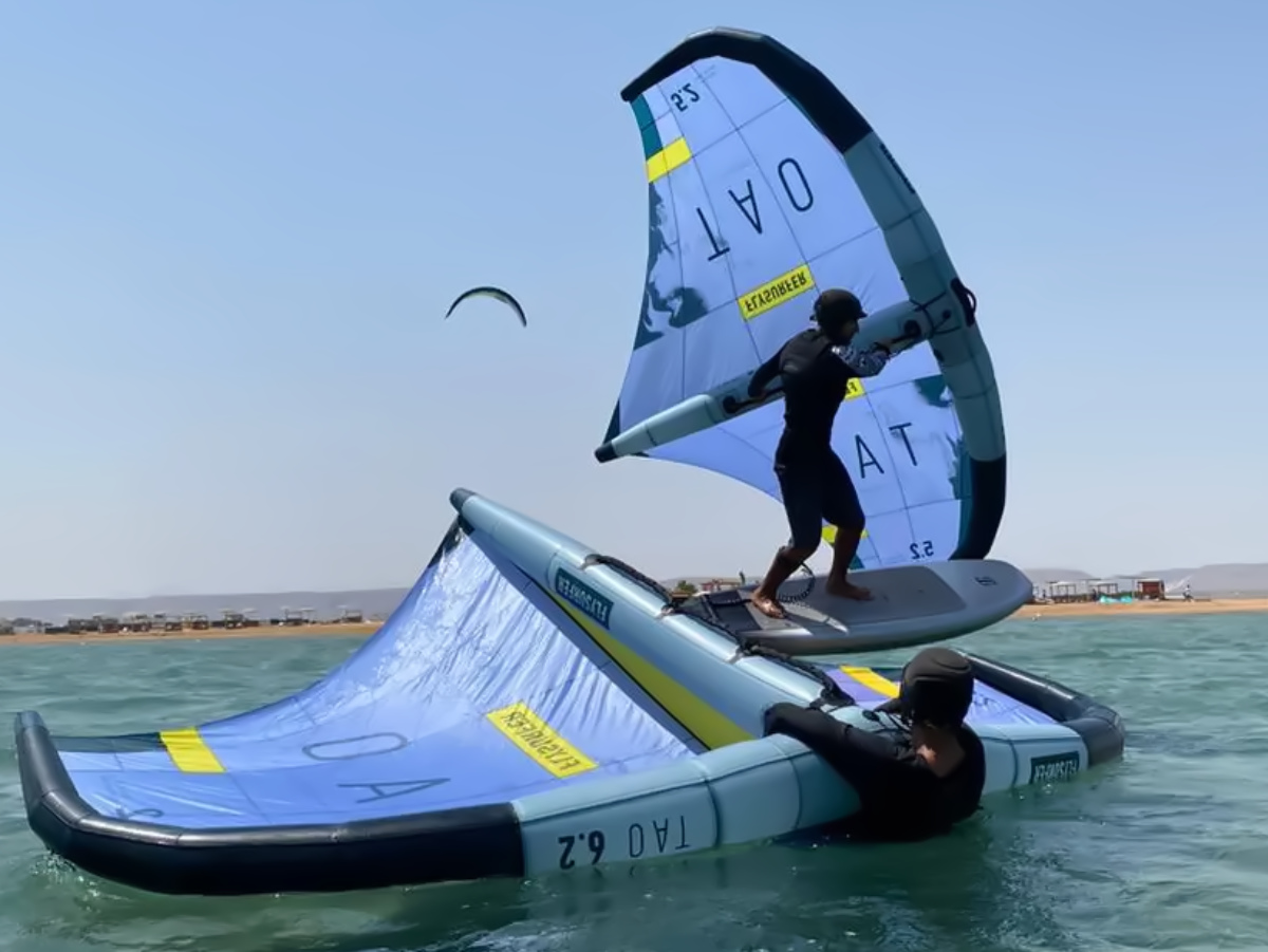 wingfoil_Course group of 5 girls sitting on the kite beach in El Gouna in Egypt, looking at the kites in the water. The image shows the girls from the back, all wearing a Kite Tribe T-Shirt